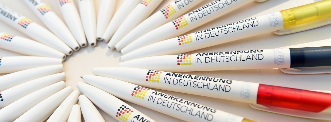 Foto de bolígrafos con el logotipo de «Anerkennung in Deutschland» impreso en ellos y dispuestos en círculo.