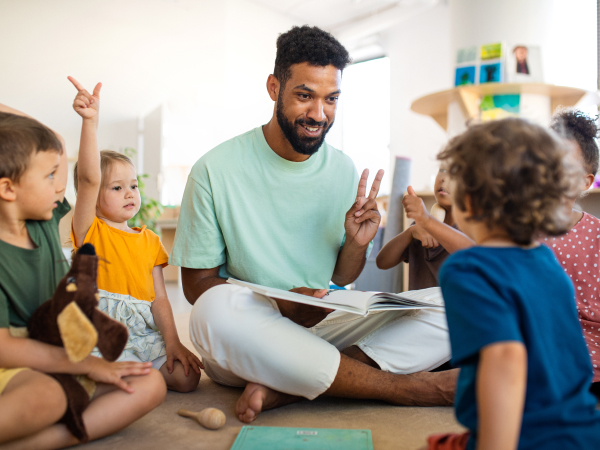 Männliche Pflegekraft liest einer Gruppe Kinder etwas vor